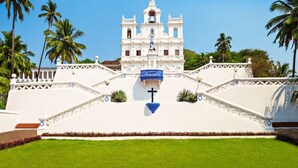 A white colonial-style building with a bell tower, surrounded by palm trees and a well-maintained lawn. - La Maison by Dia Hotels and Homes (Panaji)