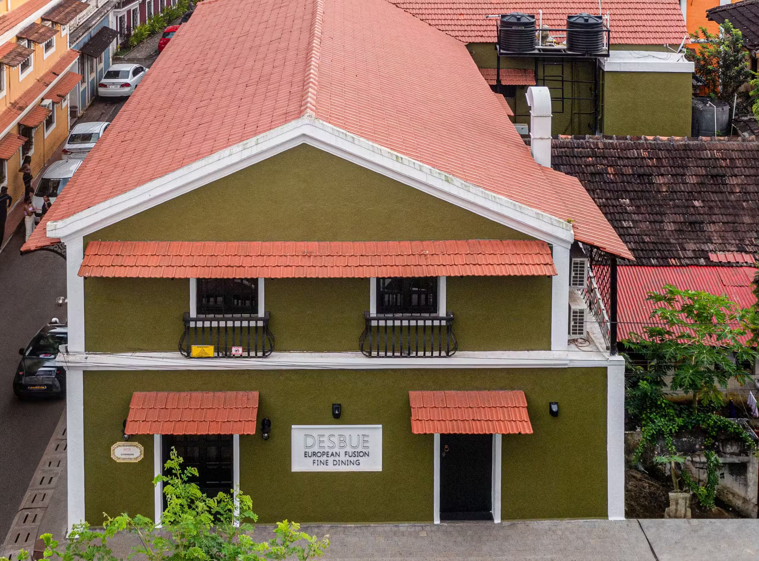 A two-story building with a red-tiled roof, a sign indicating 'DESBUE EUROPEAN FINE DINING,' and a small balcony with a railing.