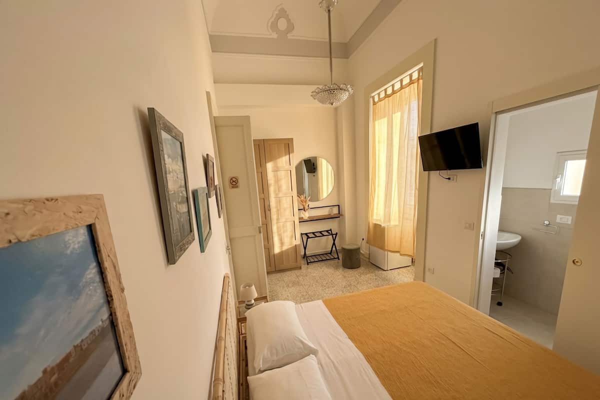 A bedroom with a bed, a TV, a mirror, and a bathroom visible through an open door.