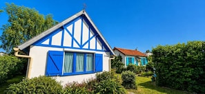 A traditional half-timbered house with a steep gable roof, a small garden, and a clear blue sky.
