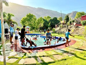 A swimming pool with people around it, surrounded by greenery and hills in the background.