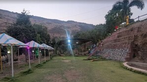 Un espacio al aire libre con un campo cubierto de césped, un muro de ladrillo y una estructura techada con luces de colores.