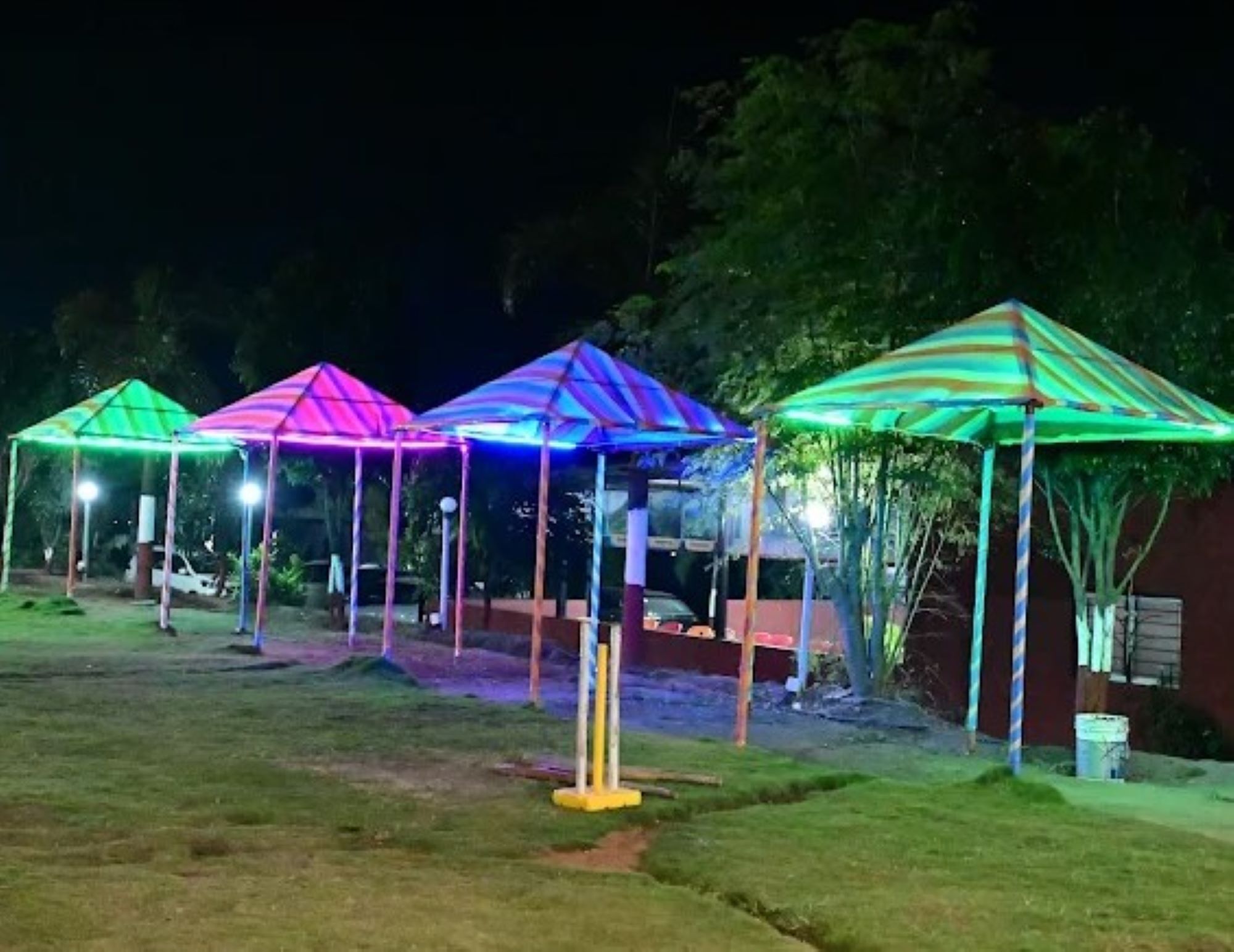 A row of brightly lit, striped canopies in a garden setting at night.