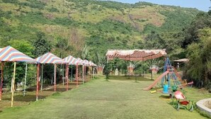 Un espacio cubierto de césped con toldos a rayas coloridas y un parque infantil con toboganes y columpios.