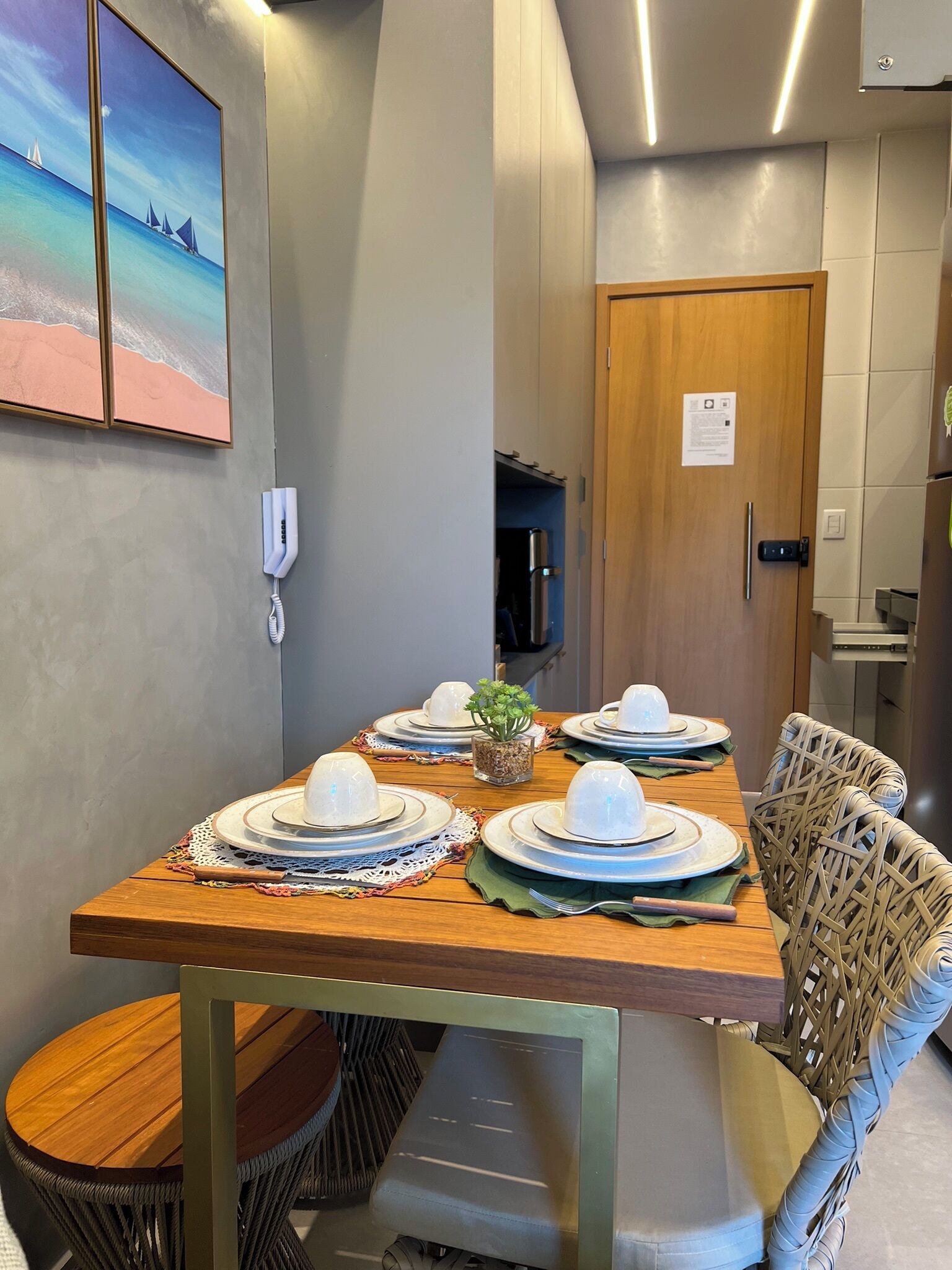 A dining area with a wooden table set for four, a wicker chair, and a small potted plant.