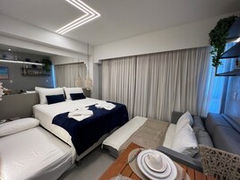 Quarto de hotel moderno com uma cama grande, um sofá e uma mesa de jantar posta com pratos e uma xícara.