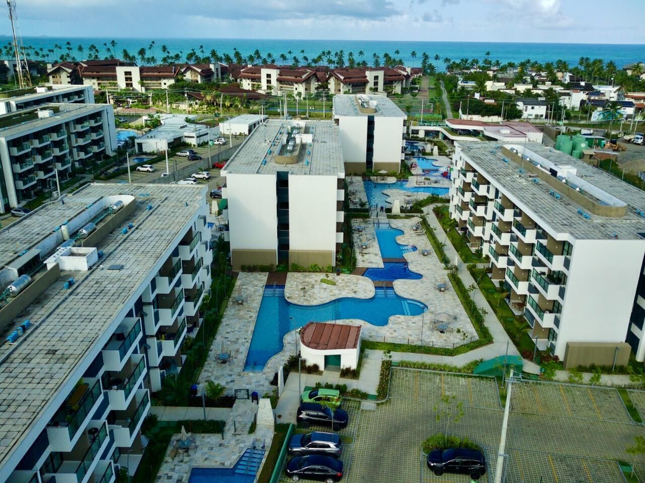 A hotel complex with multiple buildings, a swimming pool, and a view of the ocean.