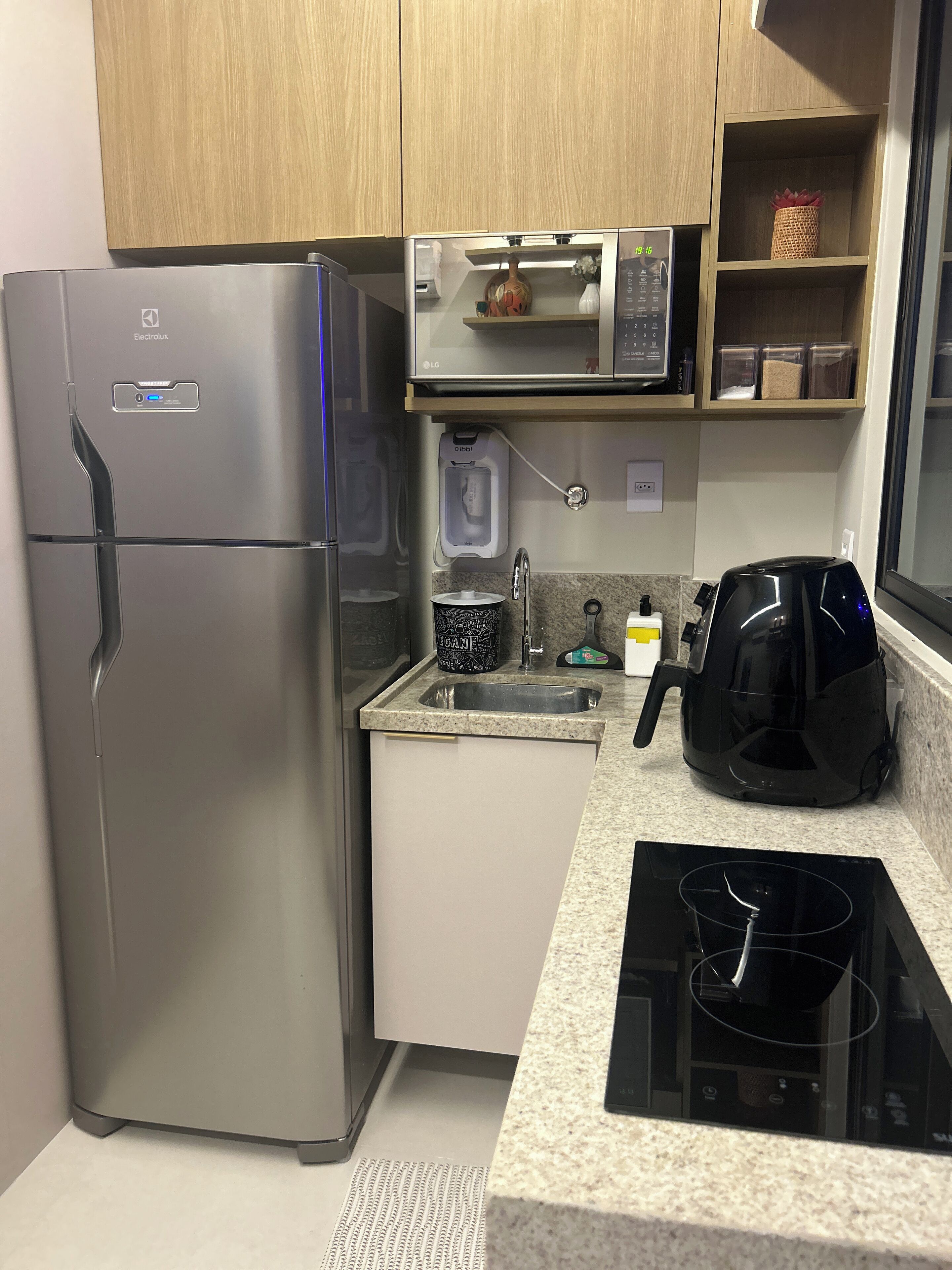 Una cocina compacta con un refrigerador de acero inoxidable, un microondas, una cafetera y un hervidor.