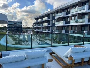 A modern hotel with a rooftop pool area, multiple balconies, and a view of the surrounding landscape.