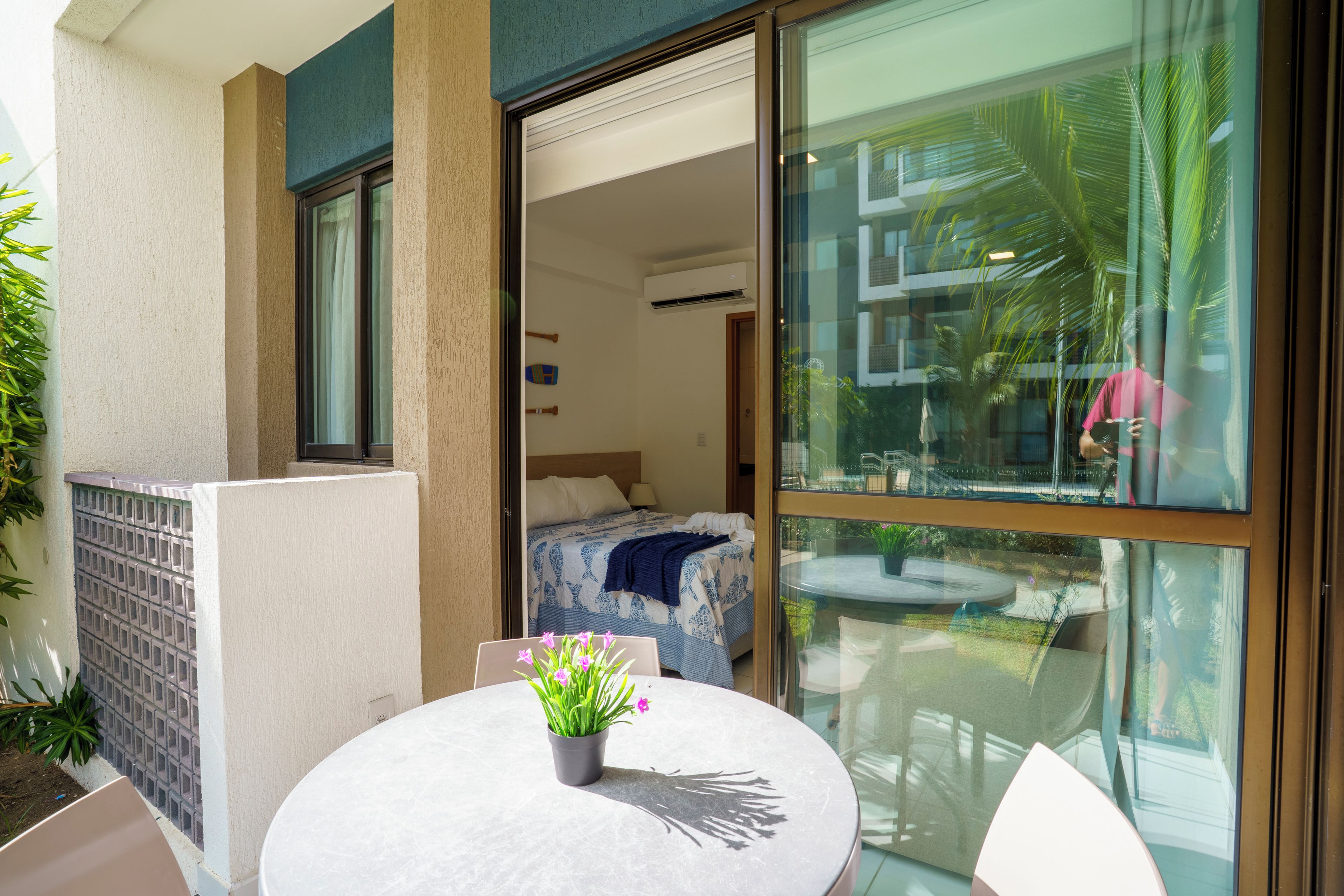 A hotel room with a bed, a small balcony with a table and chairs, and a view of the outside.