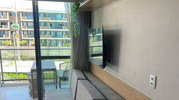 A modern living room with a sofa, a dining table set with blue plates and a wine glass, and a TV mounted on the wall.