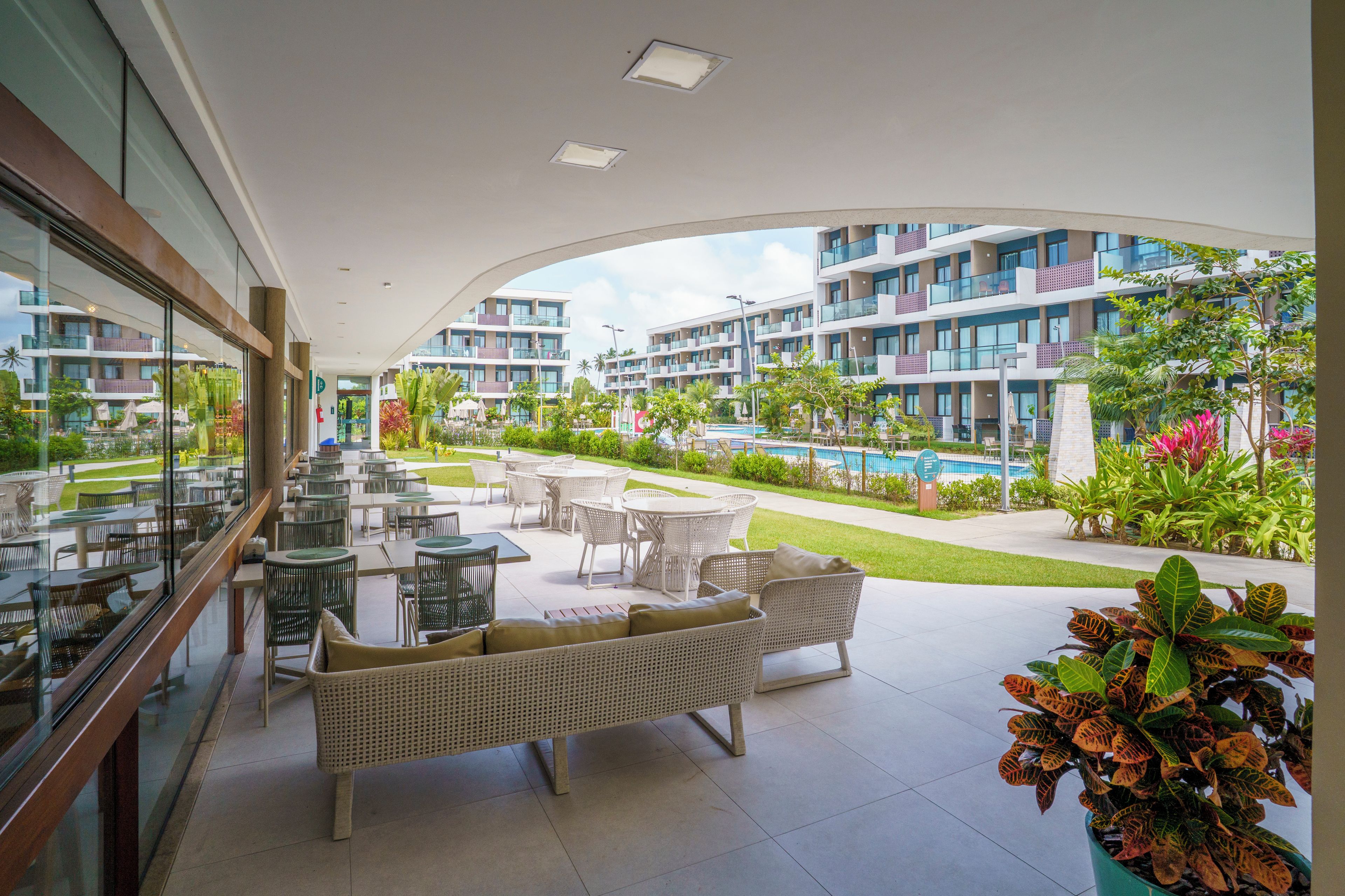 A hotel balcony with outdoor seating, a swimming pool, and a view of the hotel buildings.