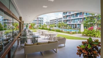 A hotel balcony with outdoor seating, a swimming pool, and a view of the hotel buildings.