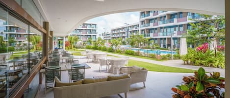 A hotel balcony with outdoor seating, a swimming pool, and a view of the hotel buildings.