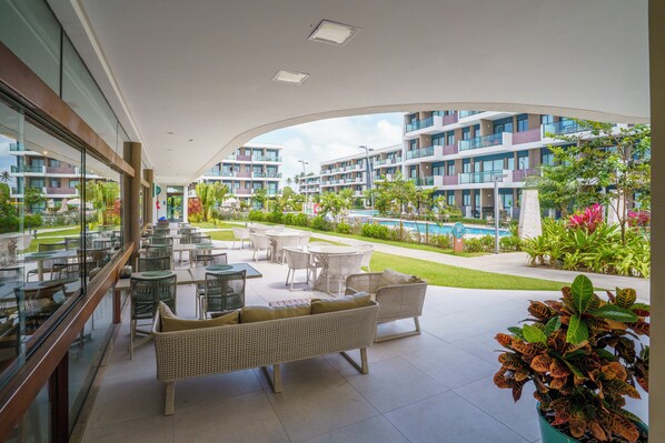 A hotel balcony with outdoor seating, a swimming pool, and a view of the hotel buildings.