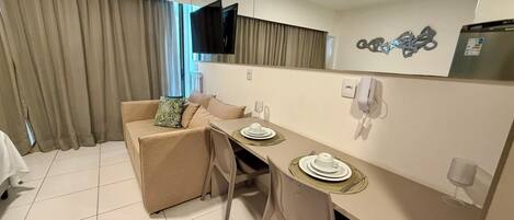 A modern hotel room with a dining area, a sofa, a flat-screen TV, a telephone, and a refrigerator.
