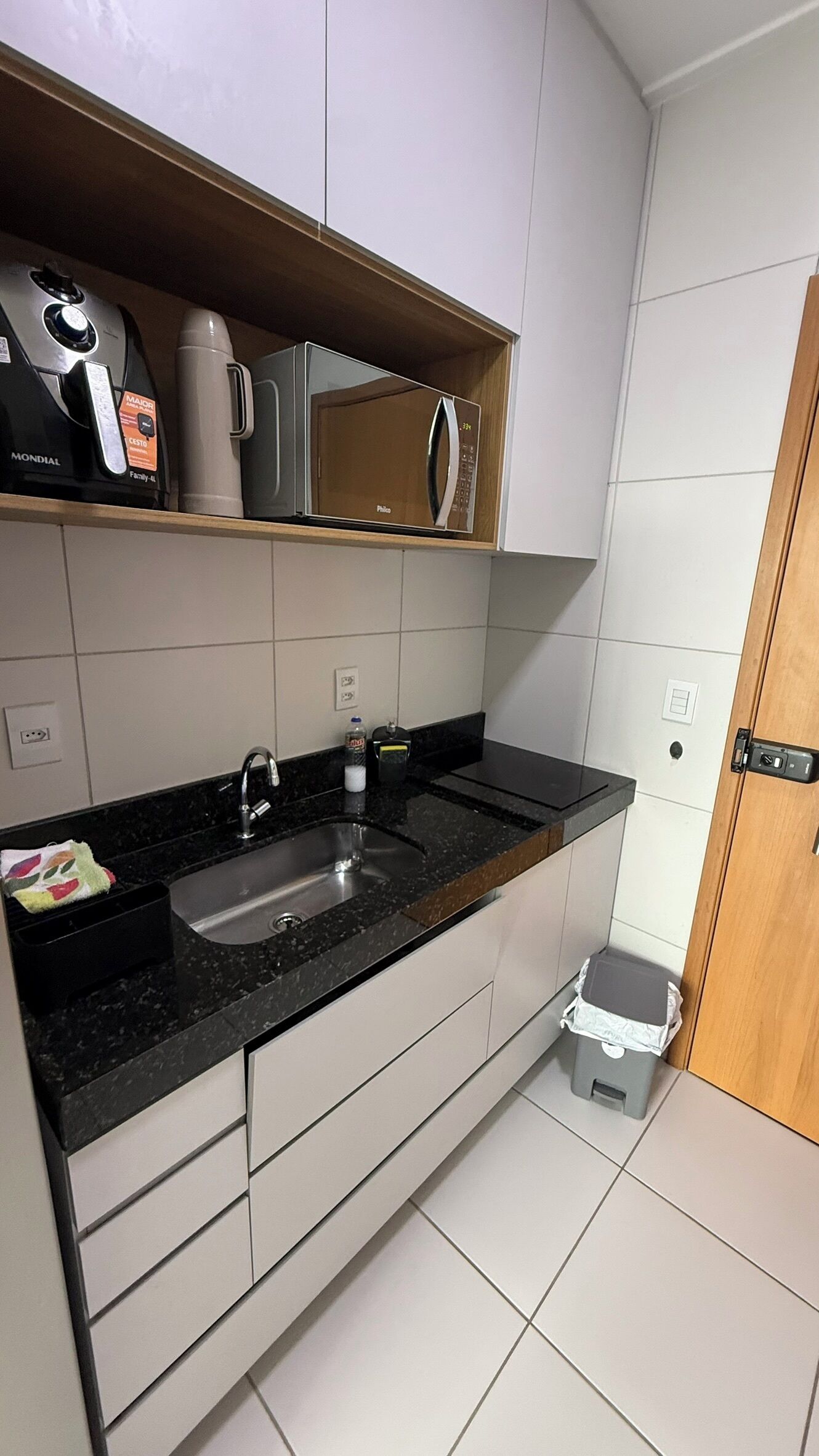 Een keuken met een zwart aanrecht, een spoelbak, een magnetron en een prullenbak.