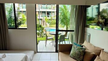 Habitación de hotel con cama, sofá, televisión y vistas a una piscina exterior y zonas verdes.