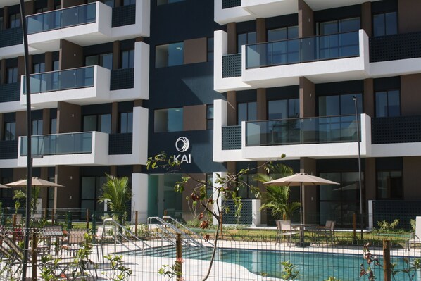 A modern hotel with a swimming pool, outdoor seating, and a sign with the logo "KAI".