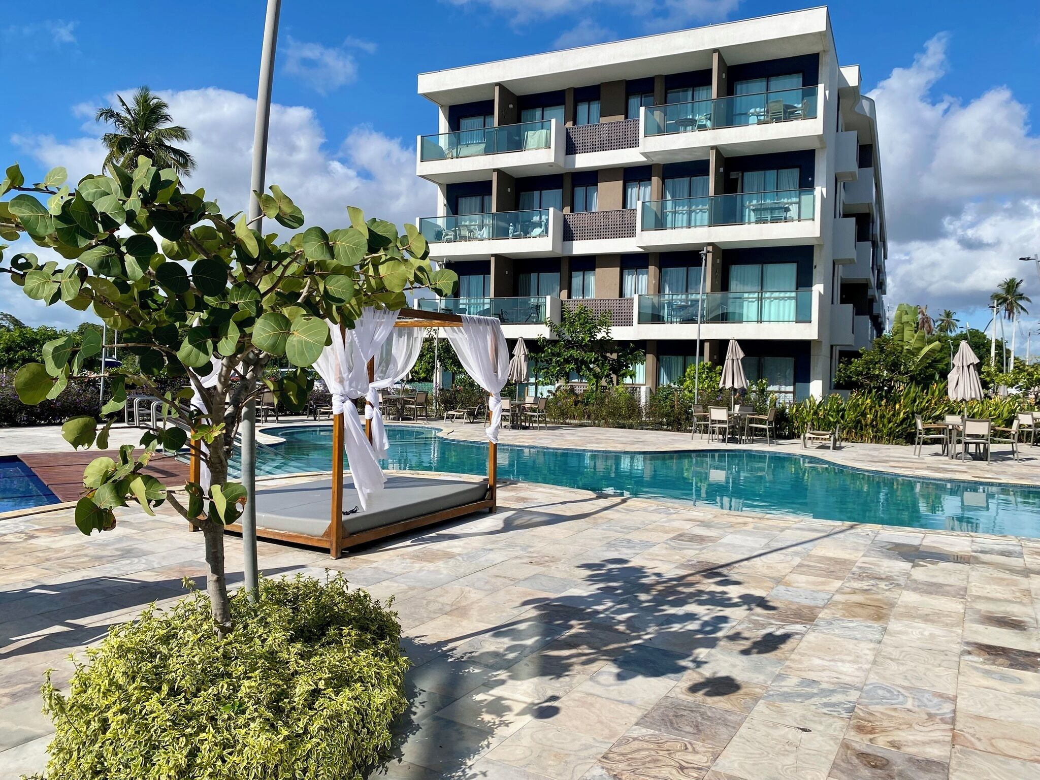 A hotel with a pool, a covered seating area, and a multi-story building with balconies.