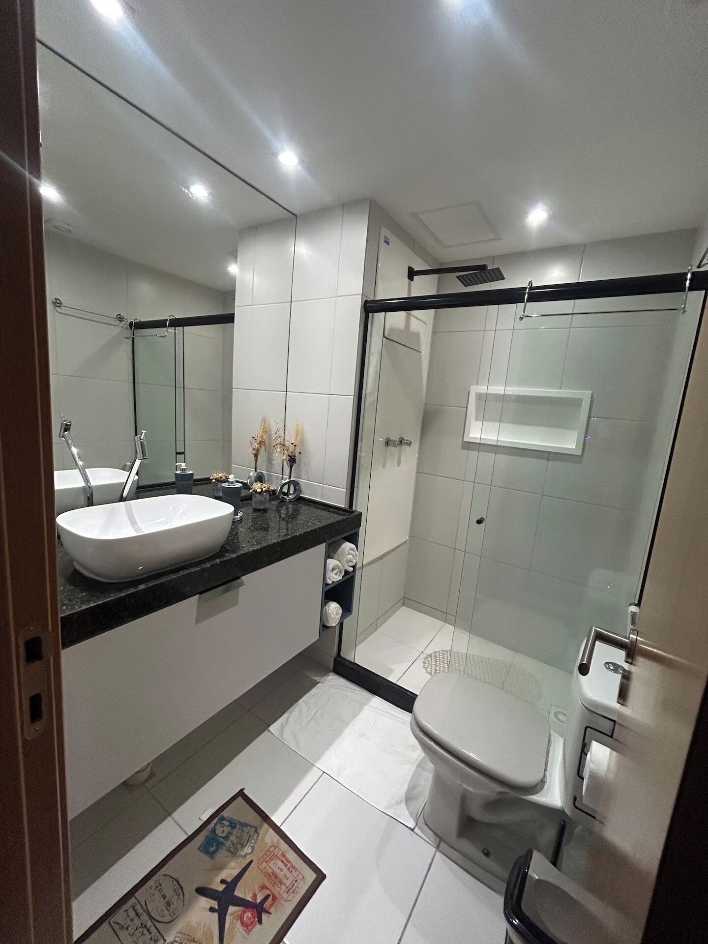 A modern bathroom with a large mirror, a white sink, a toilet, and a glass shower enclosure.