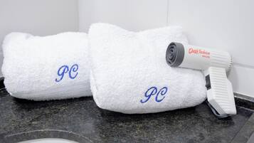 Two white towels with embroidered initials on a granite countertop, a hair dryer, and a white wall in the background.