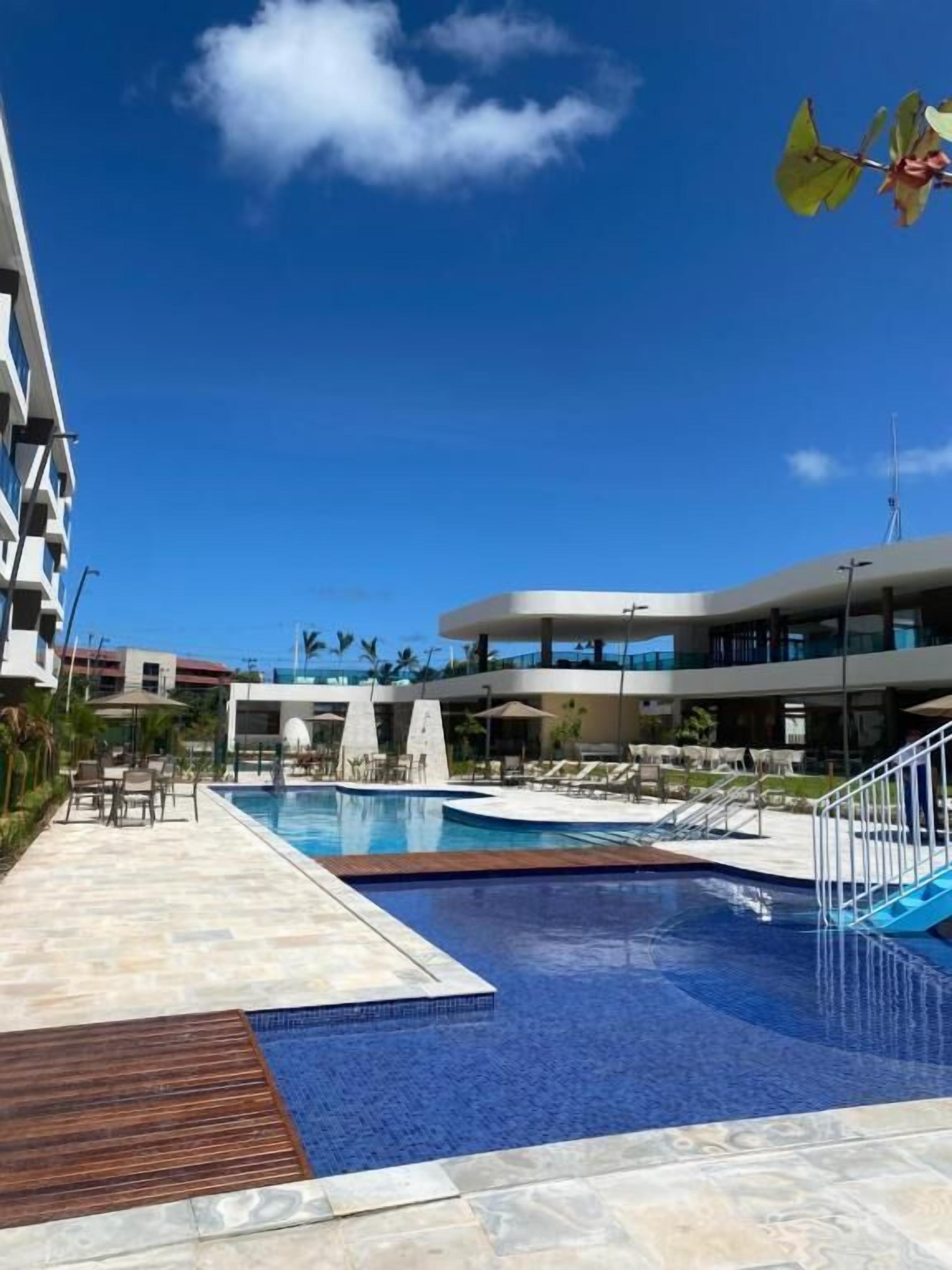 A modern hotel with a swimming pool, outdoor seating, and a clear blue sky.