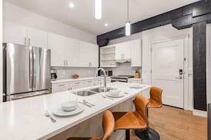 Una cocina moderna con electrodomésticos de acero inoxidable, armarios blancos y una isla central con asientos.