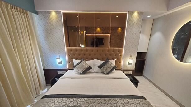 Une chambre d’hôtel moderne avec un grand lit, une tête de lit capitonnée et un miroir au-dessus du lit.