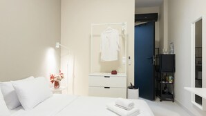 A modern hotel room with a neatly made bed, a bedside table with a vase of flowers, a small cabinet with a mirror, and a wardrobe. - Astra Beach Studio 5 (Pylos-Nestoras)