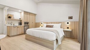 A modern bedroom with a bed, bedside tables, a built-in wardrobe, a small kitchenette, and a bathroom.