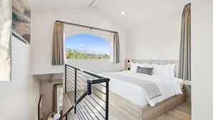 Una camera da letto con un letto grande, vista sulla vegetazione esterna e una scala che conduce a un piano superiore.
