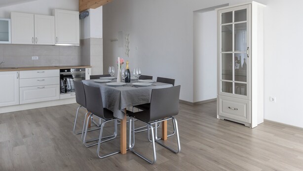 A modern kitchen with white cabinets, a dining table set for four, and a large white cabinet with glass doors. - Villa Andrea Apartments - Ljubljana (Ljubljana)