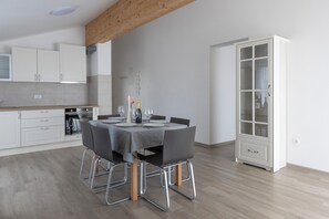 Une cuisine moderne avec des meubles blancs, une table à manger pour quatre personnes et un grand meuble blanc avec des portes en verre.