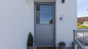 A modern grey door with a small window, a doorbell, and two potted plants on a balcony. - Villa Andrea Apartments - Ljubljana (Ljubljana)