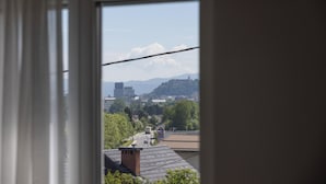 A view through a window with a clear sky, buildings, and a distant hill. - Villa Andrea Apartments - Ljubljana (Ljubljana)