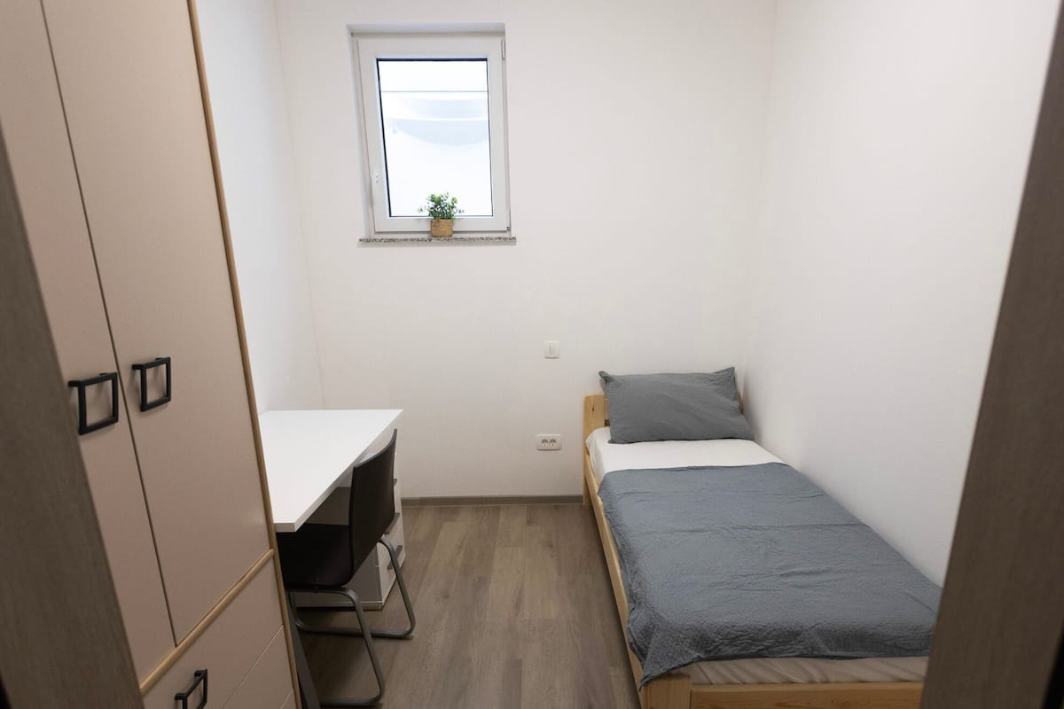 Una habitación pequeña y funcional con cama, escritorio y ventana.