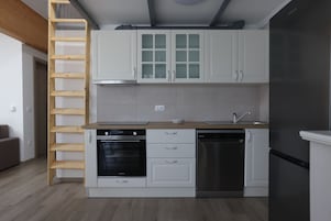 Una cocina compacta con armarios blancos, lavavajillas de acero inoxidable y una escalera de madera.