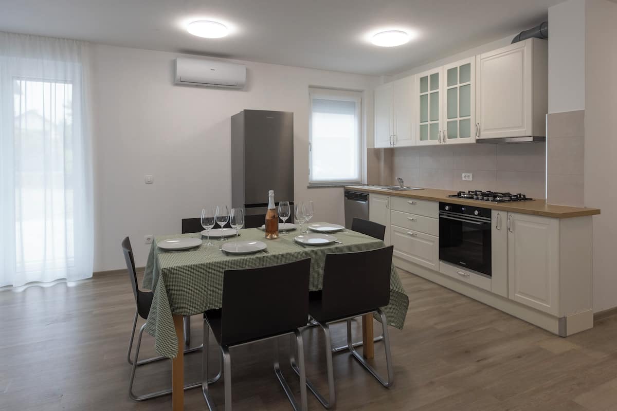 Una cocina moderna con armarios blancos, un refrigerador de acero inoxidable y un comedor con mesa dispuesta para cuatro.