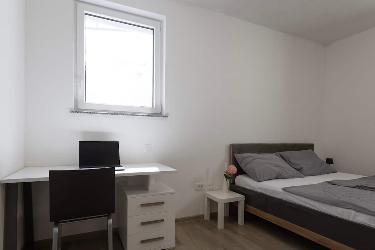 Un dormitorio con cama, escritorio, silla y ventana.