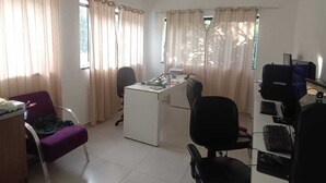 A room with a desk, two chairs, a computer, and a window with curtains. - ST DE PARNAIBA APARTMENT (Chácara do Solar II Santana de Parnaíba)