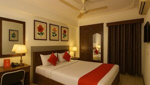 A hotel room with a large bed, two bedside tables with lamps, a desk with a chair, a wardrobe, a ceiling fan, and a TV. - The Zen Stays (Danapur)