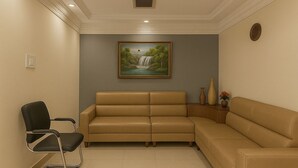 A room with a beige leather sofa, a black office chair, and a painting of a waterfall on the wall. - The Zen Stays (Danapur)