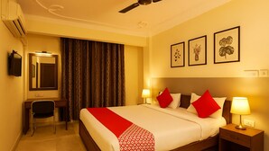 A hotel room with a bed, bedside lamps, a desk with a chair, a mirror, and curtains. - The Zen Stays (Danapur)