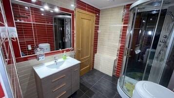 Un baño con lavamanos blanco, mueble de madera y cabina de ducha de vidrio.