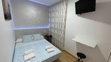 A small, modern bedroom with a bed, a TV mounted on the wall, and a small table.