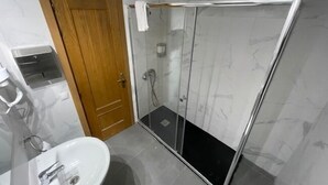 A bathroom with a wooden door, a glass shower enclosure, and a white sink.