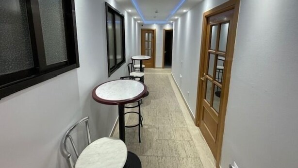 A narrow hallway with two round tables and chairs, wooden doors, and recessed ceiling lighting.