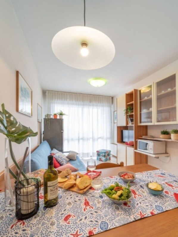 Ein modernes Wohnzimmer mit Esstisch, gedecktem Tisch für eine Mahlzeit, einer Couch und einer Küchenzeile mit Schränken und einer Mikrowelle.