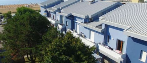 A row of modern, light blue buildings with flat roofs, likely part of a hotel or resort, overlooking a beach and the sea.